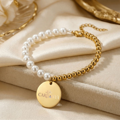 Cardanya Mother of Pearl and gold bead bracelet with personalized engraved coin pendant, displayed on luxury beige silk.